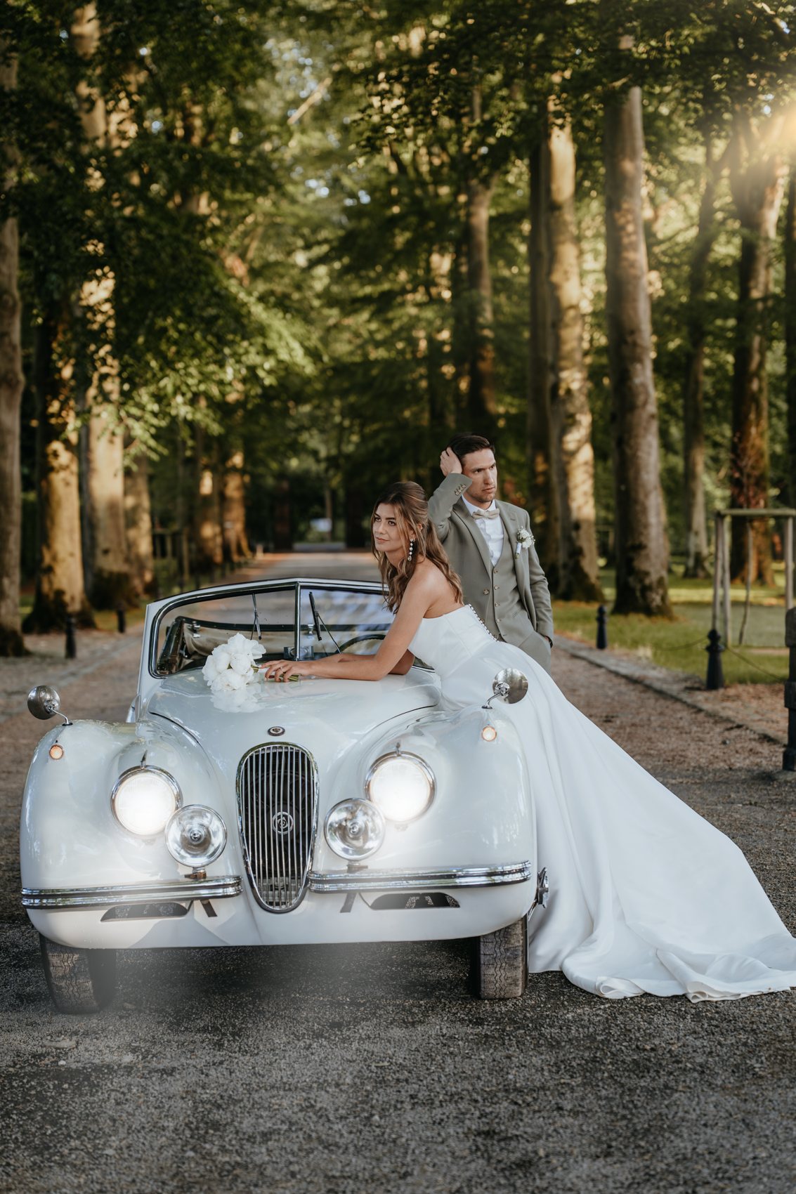 Agathe et Valentin appuyés sur le cabriolet blanc dans l’allée du château